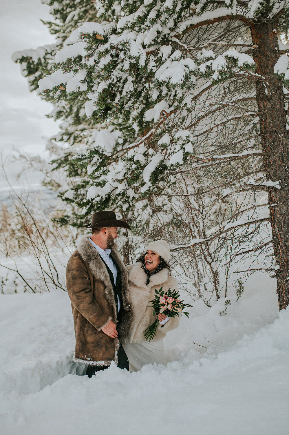 Bride and groom under a snowy tree in a forest on the day of their winter elopement in Alta Norway