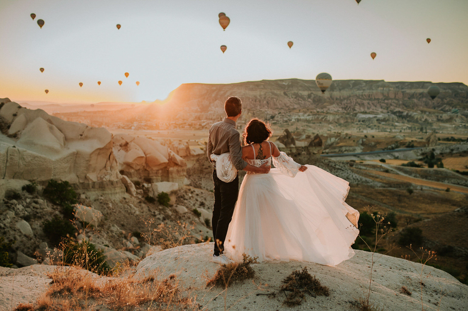 Bride and groom having an intimate moment together at sunrise in Cappadocia Turkey with hot air balloons flying in the background