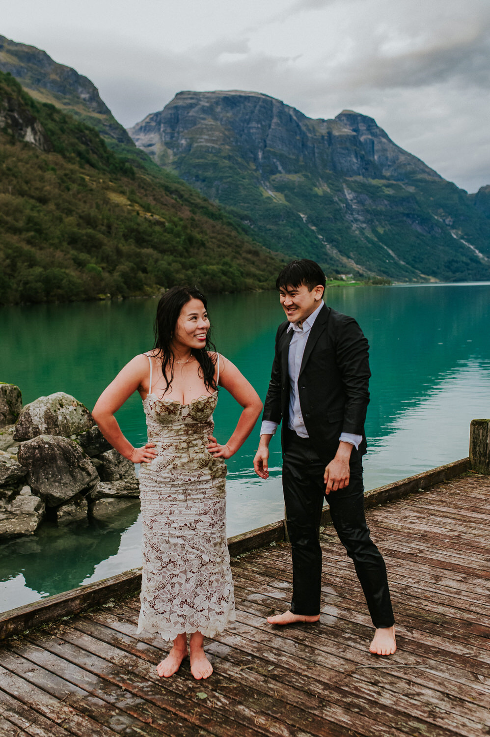 Soaking wet bride and groom in dirty wedding attire in front of Lovatnet lake in Loen Norway on the day of their adventure elopement