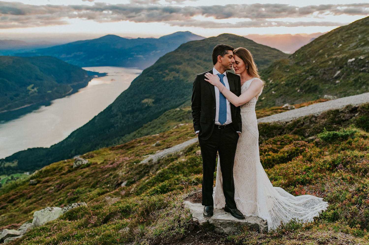 Bride and groom hugging each other on a mountaintop in Loen Norway while the sun setting down over the fjord