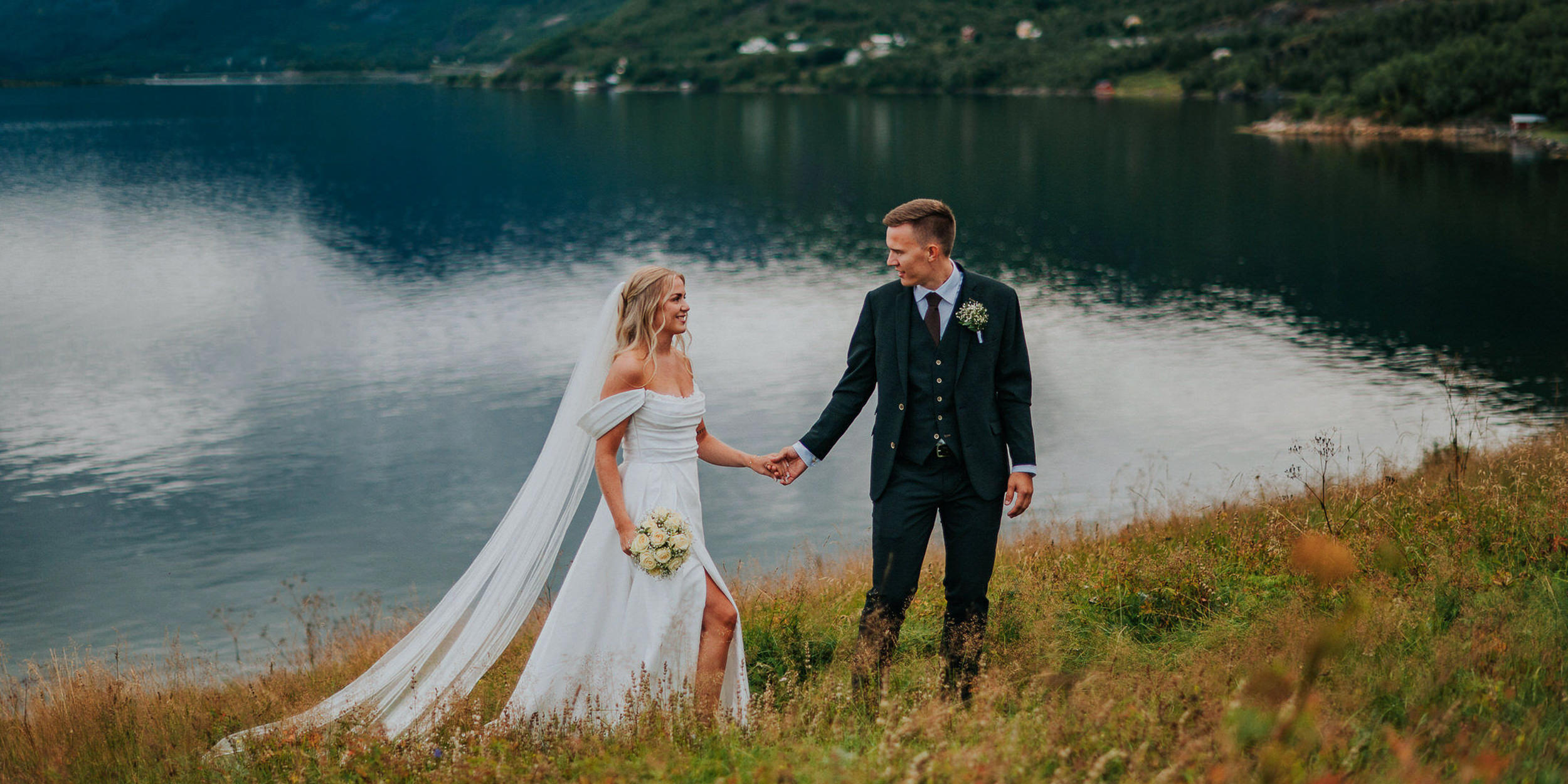 Et vakkert brudepar spaserer foran en fjord i Alta på bryllupsdagen sin