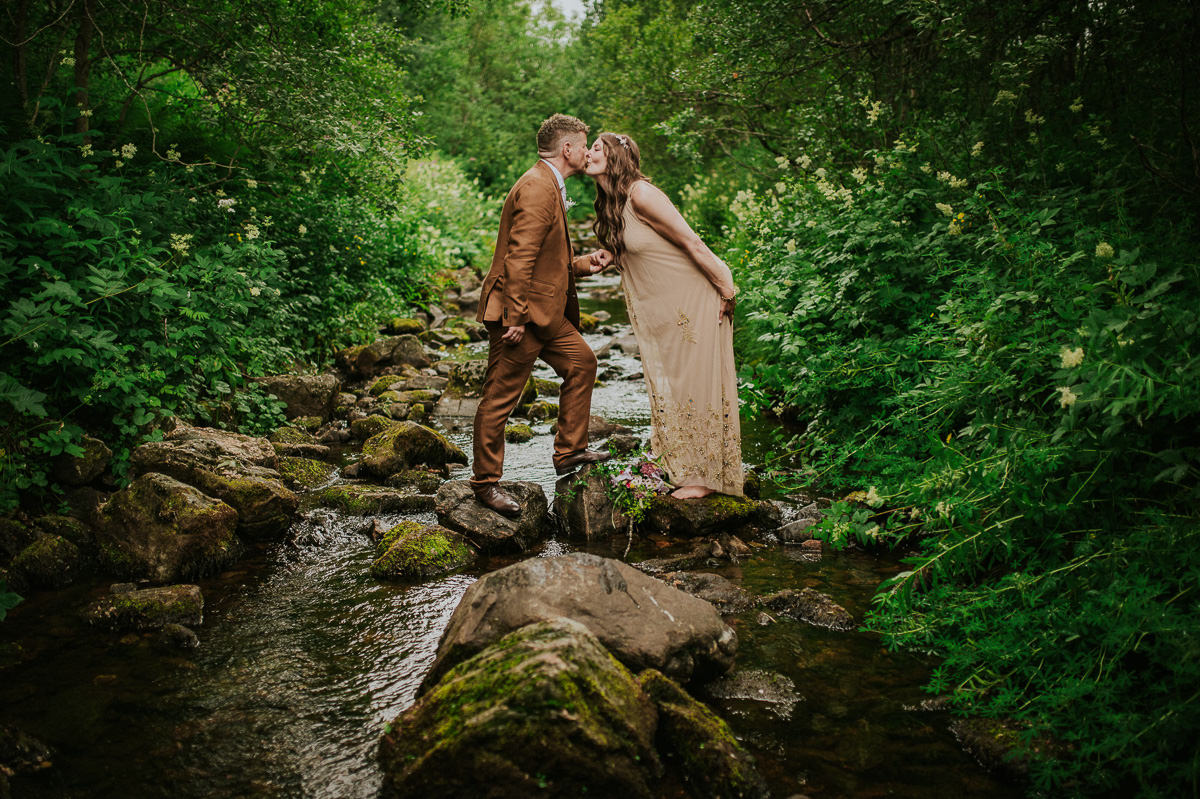 Et nydelig bohemsk brudepar står i bekken i en skog i Vesterålen på bryllupsdagen sin