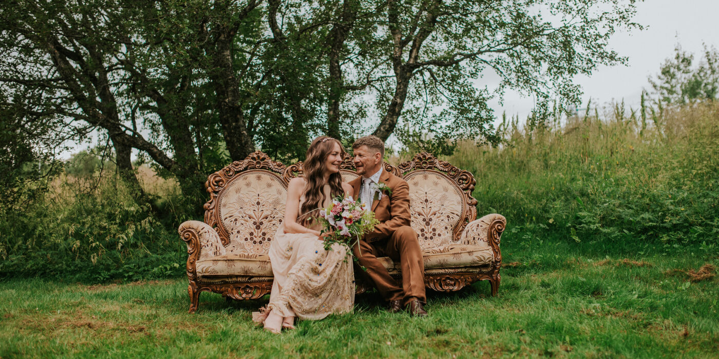Bohemsk brudepar i vintage bryllupsklær sitter på en antikk sofa i skogen i Sortland Vesterålen på bryllupsdagen sin