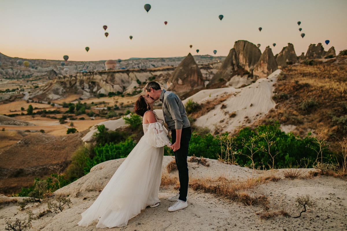Bride and groom at dawn in Cappadocia watching hot air balloons drift in the sky