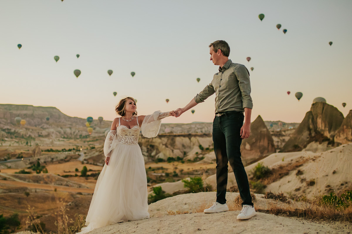 Bride and groom at dawn in Cappadocia watching hot air balloons drift in the sky