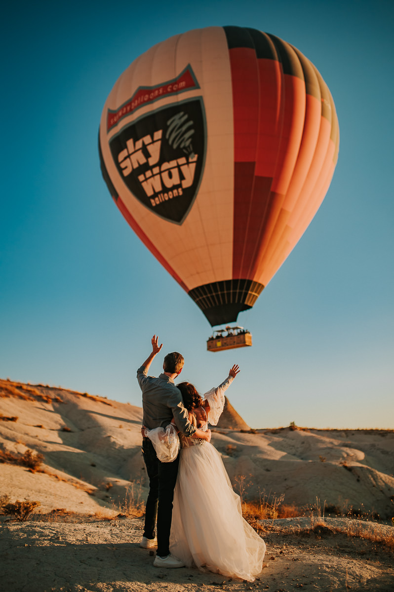 Bride and groom waving at a hot air balloon in Cappadocia on their wedding day