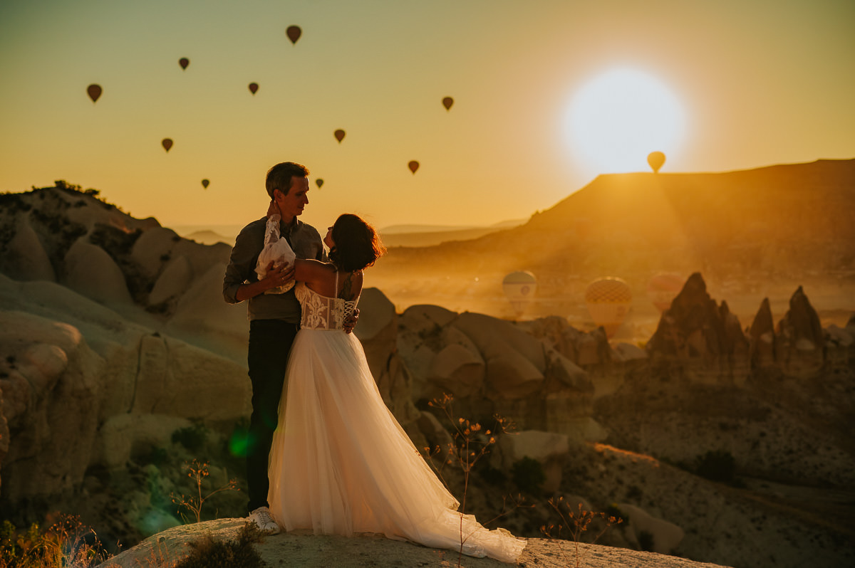 Bride and groom watching a stunning sunrise and hot air balloons drifting in the sky in Cappadocia on the day of their elopement
