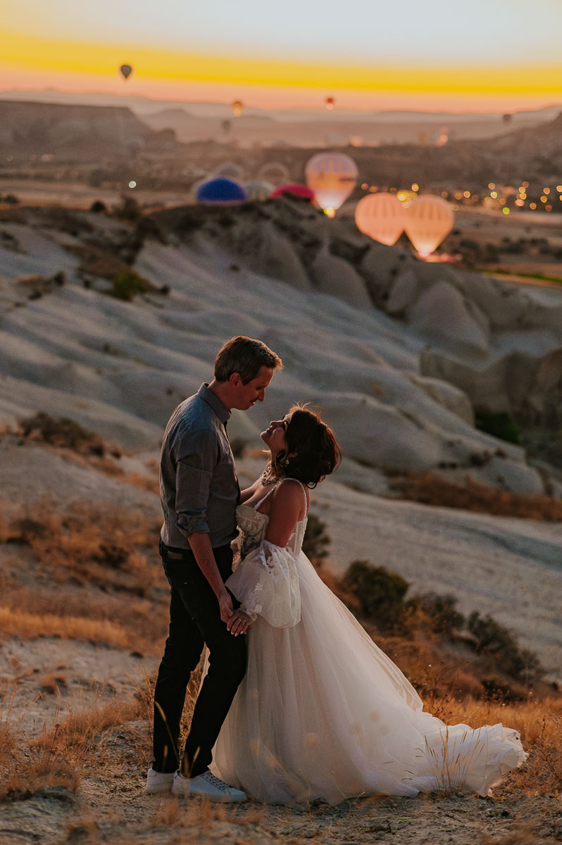 Bride and groom at dawn in Cappadocia watching hot air balloons drift in the sky