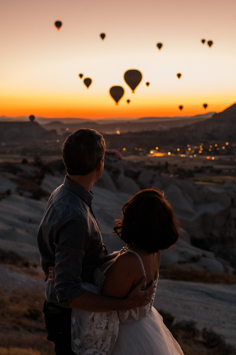 Bride and groom watching gorgeous dawn with hot air balloons in Cappadocia Turkey with red and purple sky