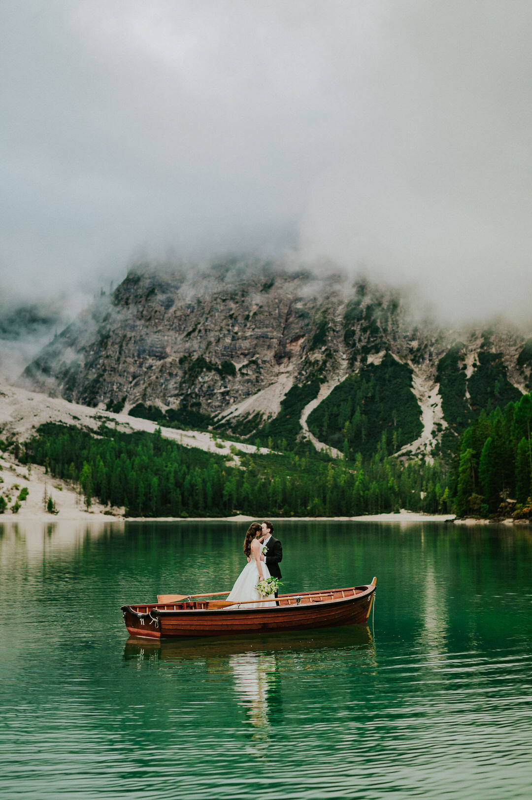 Bride and groom rowing an old wooden boat at Lago di Braies in the Italian Dolomites on the day of their adventure elopement - captured by elopement photographer TS Foto Design