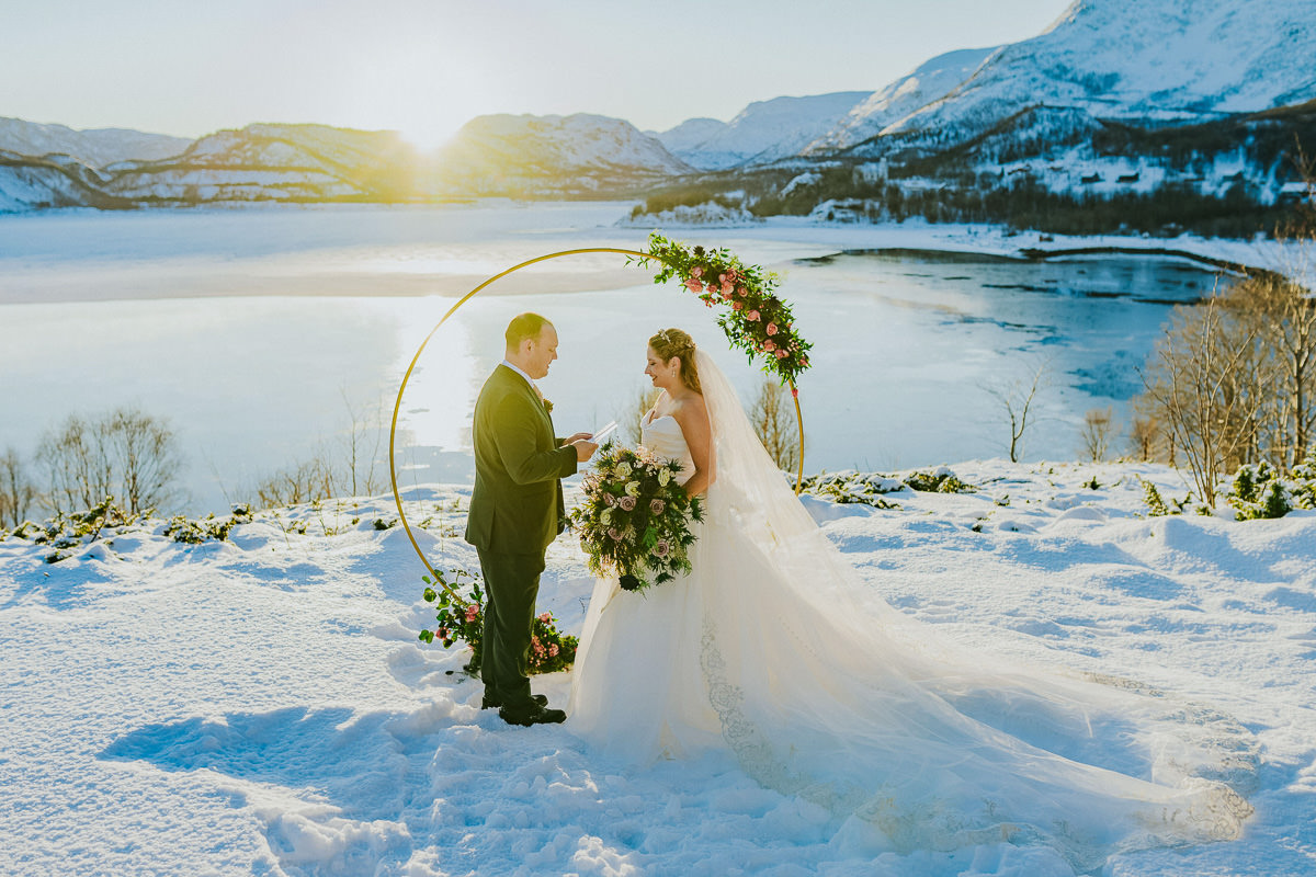 Stunning arctic winter wedding ceremony in front of a  circular wedding arch decorated with roses and greenery with in Alta Norway 