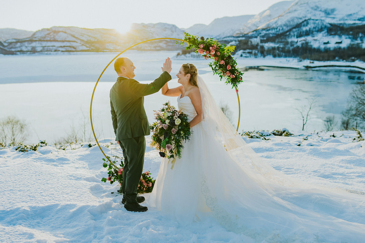 Bride and groom raised their hands in a high five right after their wedding ceremony in Alta Norway. There is a gorgeous arctic landscape in the background with the mountains and the fjord