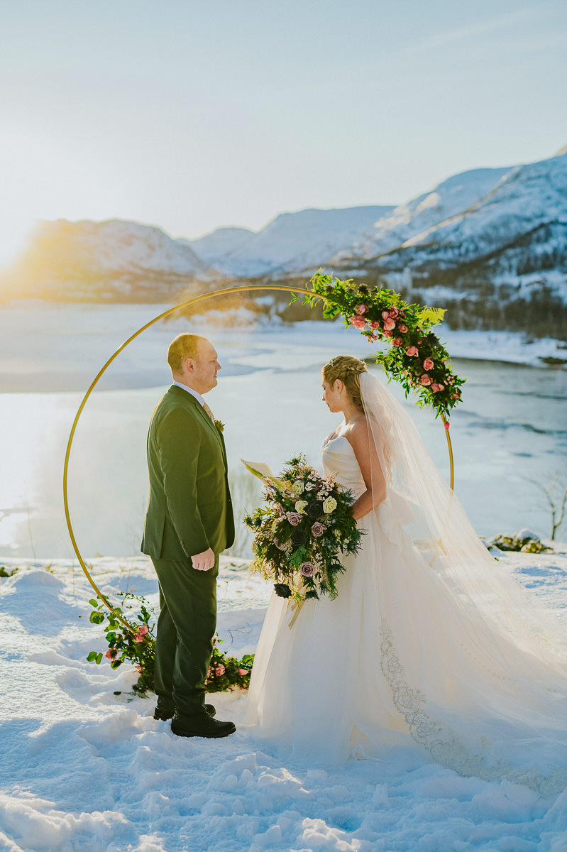 Stunning arctic winter wedding ceremony in front of a  circular wedding arch decorated with roses and greenery with in Alta Norway 