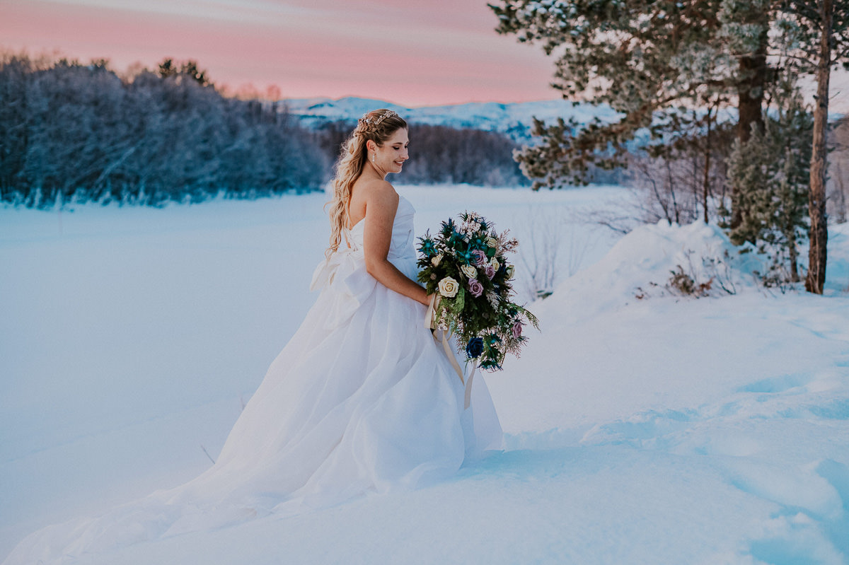 Beautiful bride posing in front of an arctic landscape with pink sky in the background