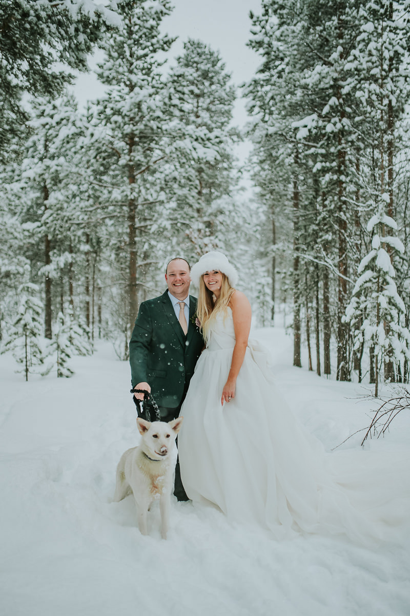 Bride and groom portrait in a snow covered forest with a white husky dog