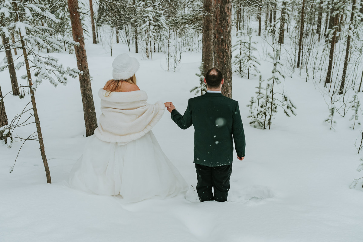 Bride and groom in their wedding attire falling in the snow in a winter forest in Alta Norway on the day of their arctic wedding