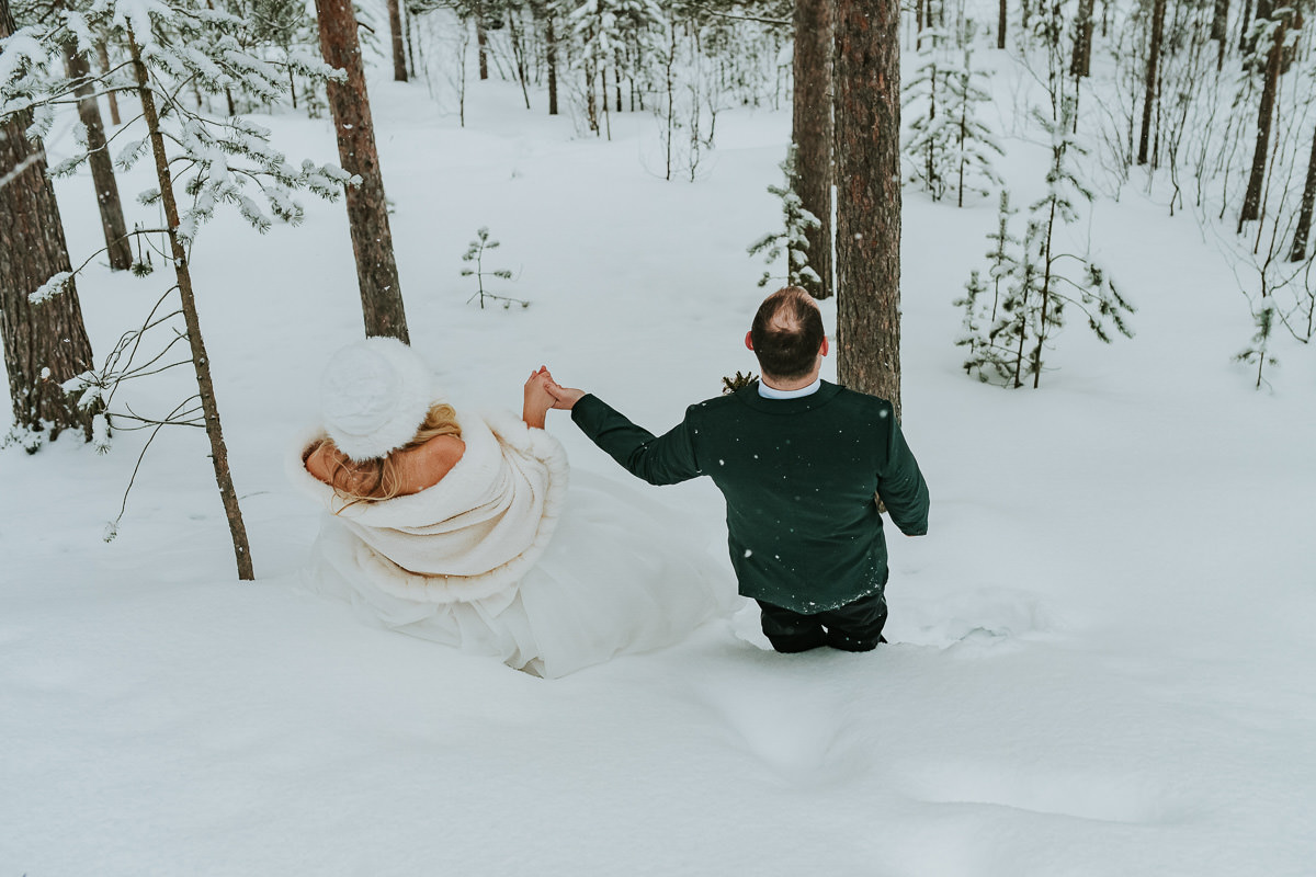Bride and groom in their wedding attire falling in the snow in a winter forest in Alta Norway on the day of their arctic wedding