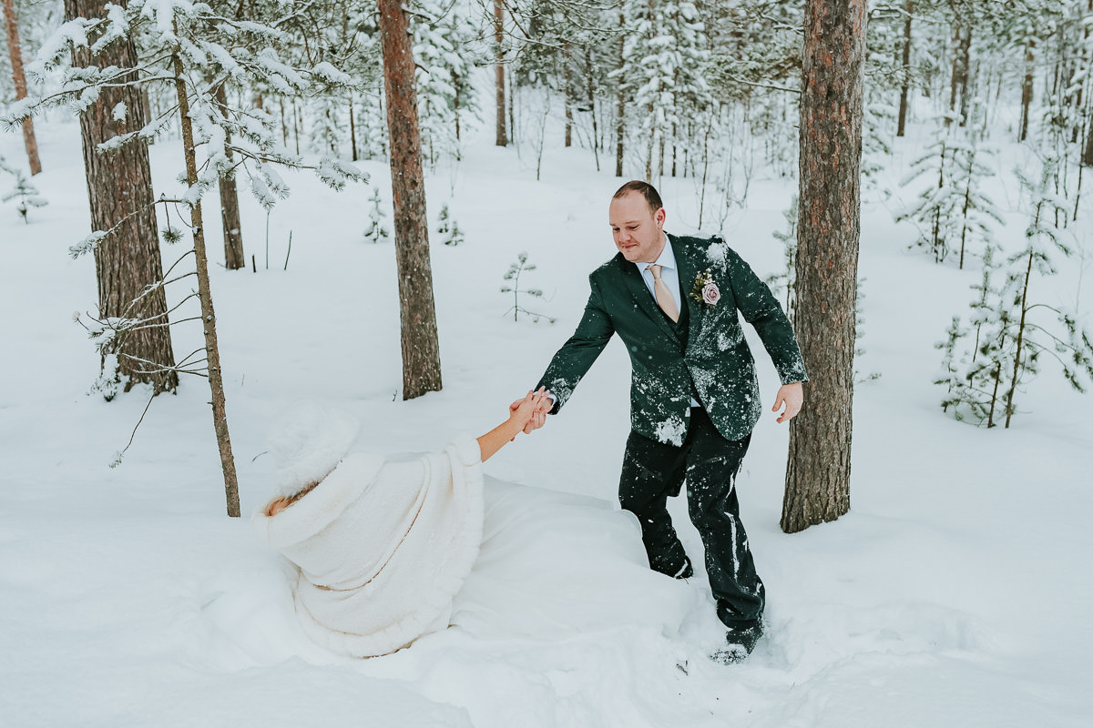 Bride and groom in their wedding attire falling in the snow in a winter forest in Alta Norway on the day of their arctic wedding