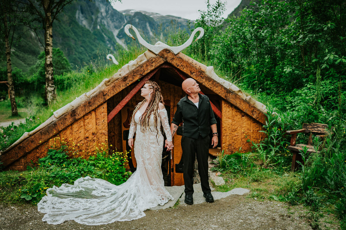 Viking themed adventure wedding in Gudvangen Norway - the couple is posing in front of a Viking house and green scenery