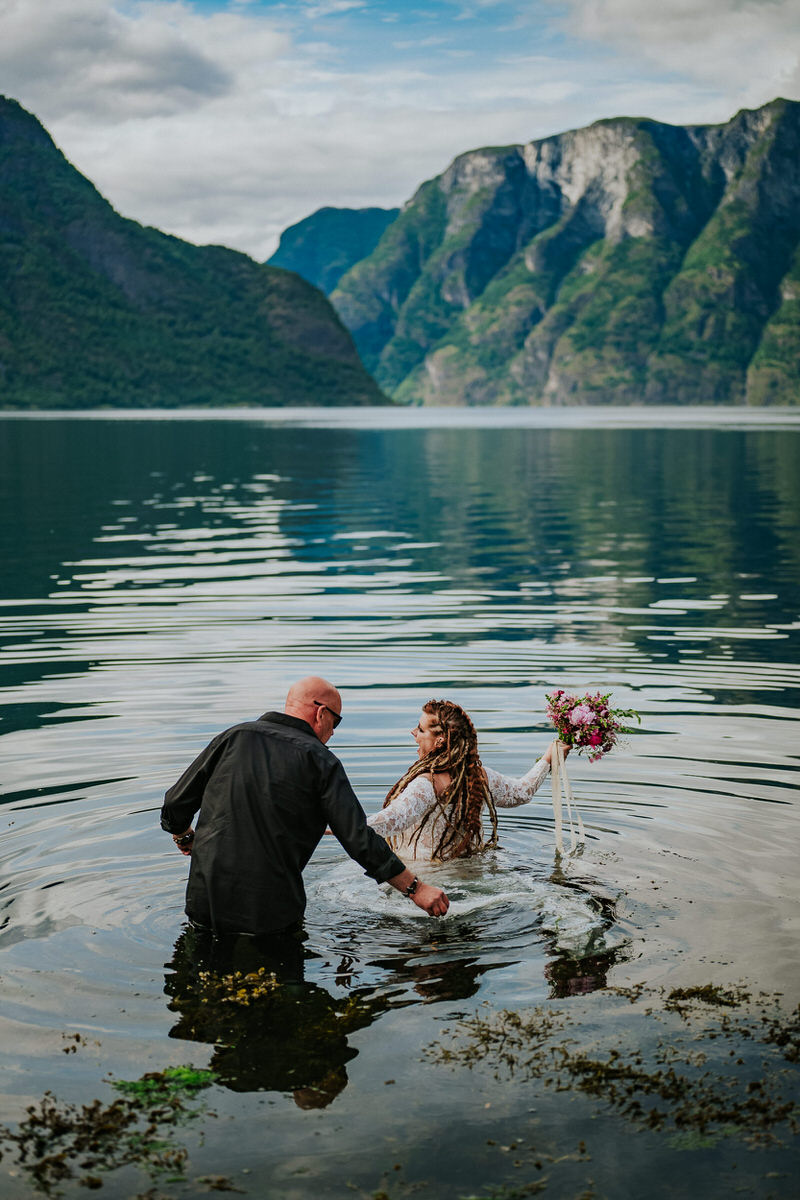 Bride and groom walking into the waters of Aurlandsfjord on the day of their adventure wedding
