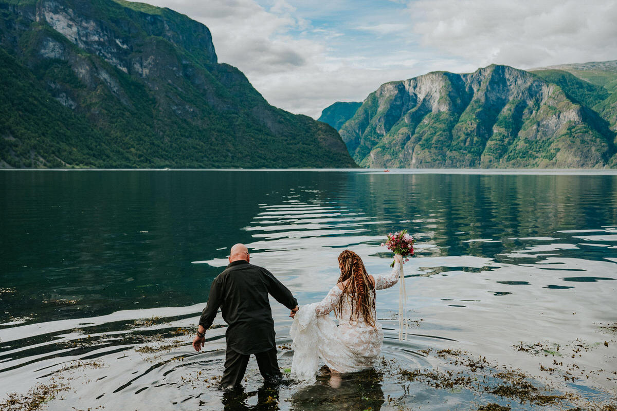 Bride and groom walking into the waters of Aurlandsfjord on the day of their adventure wedding