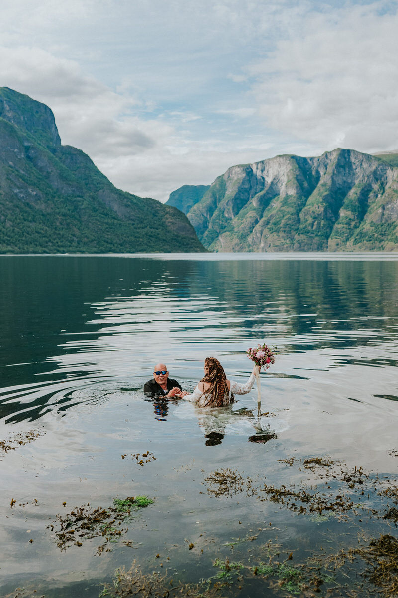 Bride and groom walking into the waters of Aurlandsfjord on the day of their adventure wedding