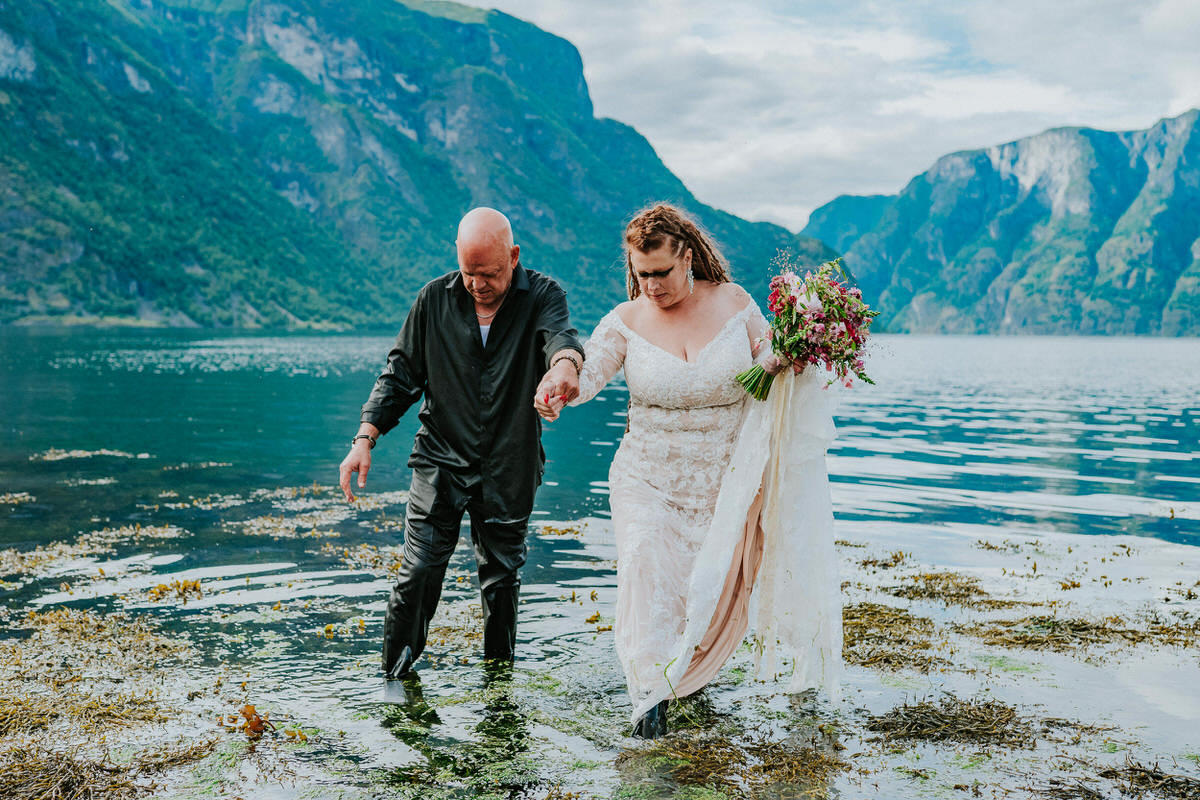 Bride and groom walking into the waters of Aurlandsfjord on the day of their adventure wedding