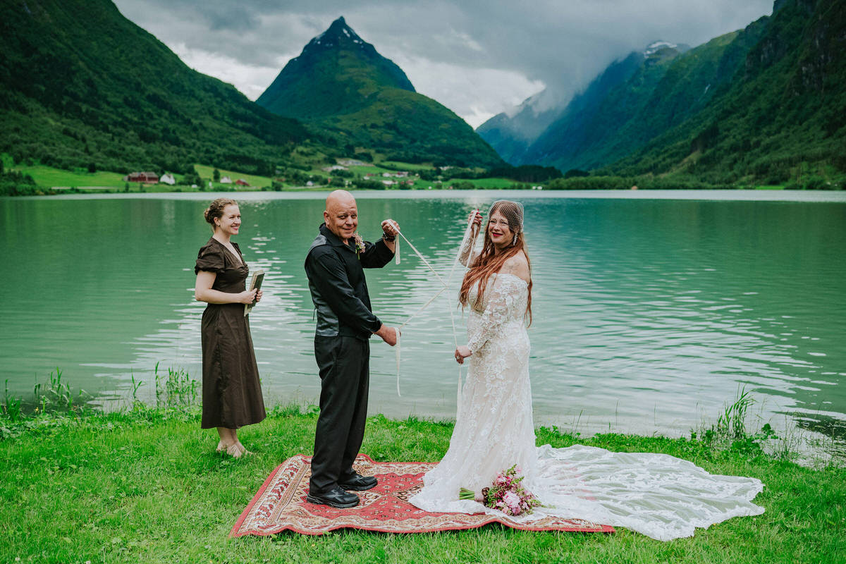 Outdoor elopement ceremony in front of a lake and Mt. Eggenipa in Western Norway - bride and groom doing handfasting