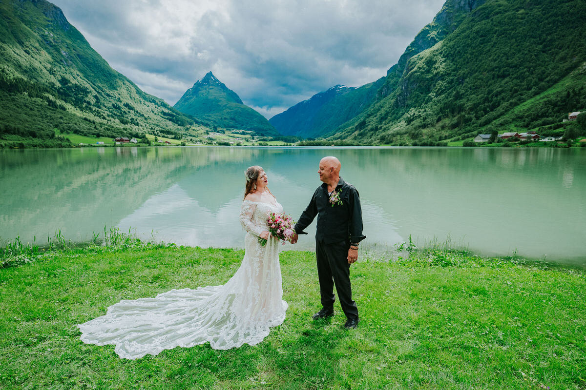 Bride and groom posing outside in front of a beautiful green lake and Mt. Eggenipa on the day of their adventure elopement in Norway