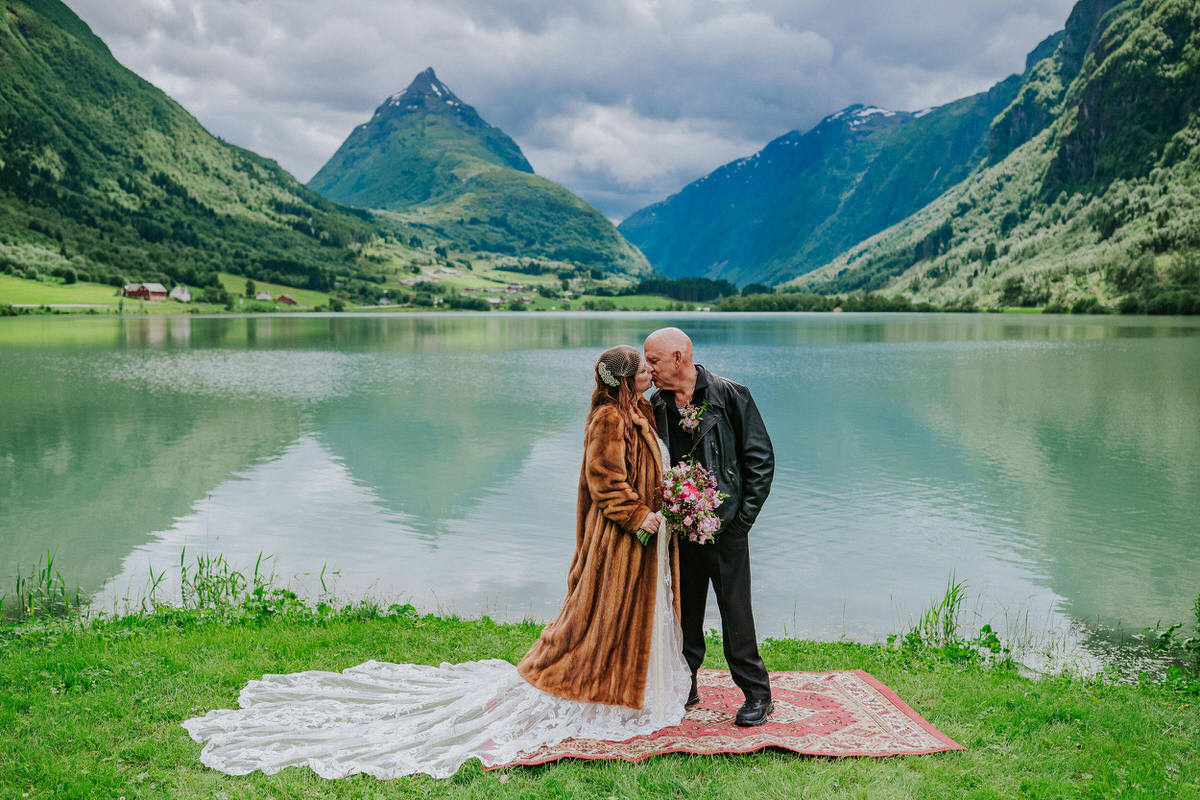 Bride and groom posing outside in front of a beautiful green lake and Mt. Eggenipa on the day of their adventure elopement in Norway