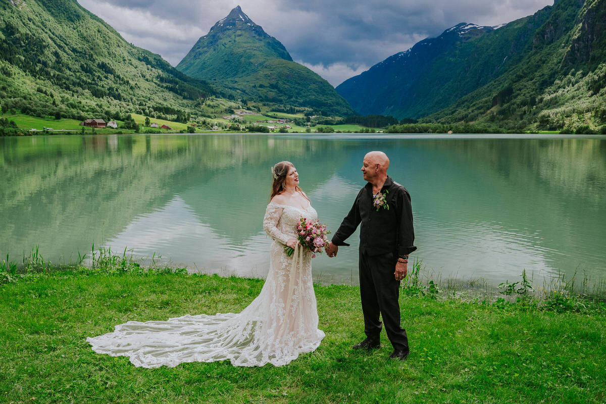 Bride and groom posing outside in front of a beautiful green lake and Mt. Eggenipa on the day of their adventure elopement in Norway