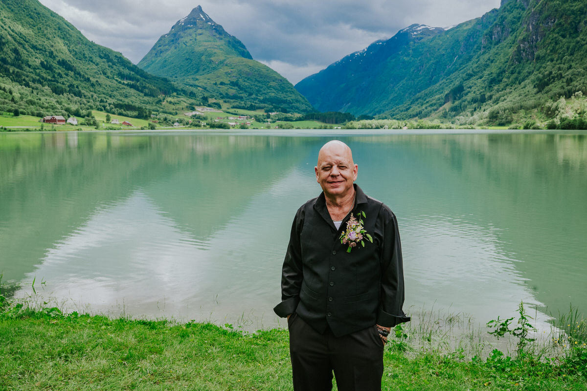 Groom posing outside in front of a beautiful green lake and Mt. Eggenipa on the day of their adventure elopement in Norway