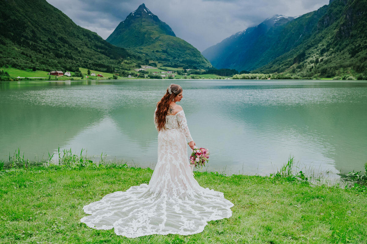 Bride posing outside in front of a beautiful green lake and Mt. Eggenipa on the day of their adventure elopement in Norway