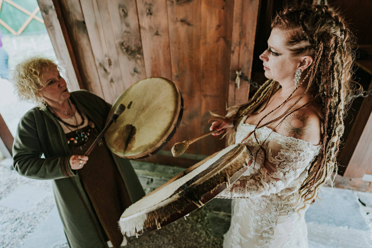 Bride with viking style hair braids playing drums in the viking village in Gudvangen Norway on the day of her viking elopement