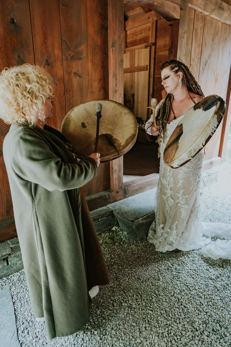 Bride with viking style hair braids playing drums in the viking village in Gudvangen Norway on the day of her viking elopement