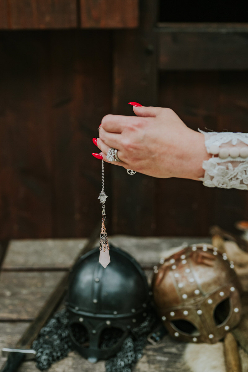 Bride holding a pendulum in front of viking helmets in Gudvangen viking village